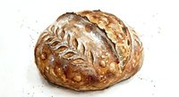 Artisan sourdough bread loaf with decorative wheat pattern and seeds on rustic speckled surface for bakery and food photography.
