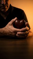Senior man holding wooden heart in protective hands with warm golden lighting for love and care concepts.