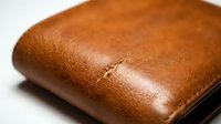 Worn leather wallet with cognac brown patina and visible creasing, displaying aged texture and craftsmanship for luxury goods, fashion, and lifestyle content.
