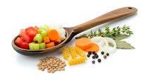 Wooden spoon with colorful diced vegetables, pasta, beans and herbs isolated on white background for healthy cooking and meal preparation.