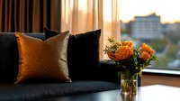 Elegant living room interior with black velvet sofa, gold and black decorative pillows, orange roses in glass vase by window during golden hour sunset.