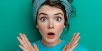 Young woman with shocked expression wearing turquoise headband against matching background, hands raised in surprise.