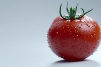 Fresh ripe red tomato with water drops and green stem on light background, macro photography showing texture and natural moisture for food design.