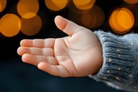 Open palm wearing gray knit sweater against dark background with golden bokeh lights creating magical winter holiday atmosphere and warm glow effect.