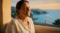 Middle-aged woman relaxing on terrace overlooking ocean at sunset, enjoying peaceful moment during vacation retreat with serene coastal view.