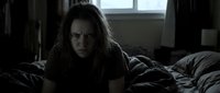 Young woman with long dark hair lying on bed in dimly lit bedroom, expressing concern or distress, suitable for dramatic storytelling, psychological themes, mental health awareness, film production, and editorial content.