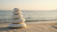 Balanced stack of smooth white stones on sandy beach at sunset creating zen meditation symbol for wellness and mindfulness practices.