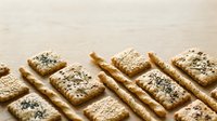 Homemade oat and sesame seed crackers arranged diagonally on wooden surface, dusted with powdered sugar for baking, snack, and food photography use.