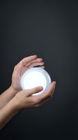 Hands protecting glowing white orb sphere against dark background symbolizing care protection energy future innovation technology concept.