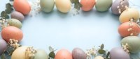 Pastel Easter eggs and delicate wildflowers arranged in an oval frame on a soft blue background, leaving copy space for seasonal greetings.