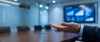 Man in business suit presenting data analytics on screen in modern conference room meeting.
