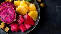 Fresh tropical fruit plate with bright pink dragon fruit and golden pineapple chunks on dark background, healthy exotic food styling for restaurant menu.