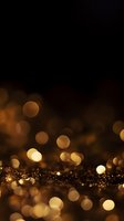 Golden glitter bokeh lights on dark background with defocused sparkles and shimmering particles creating magical festive atmosphere.