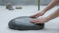 Hands touching smooth zen stone in Japanese rock garden for meditation and mindfulness practice creating peaceful atmosphere for relaxation and spiritual wellness.