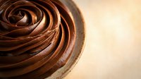 Rich chocolate frosting swirl in mixing bowl with warm golden background perfect for baking and dessert recipes.