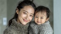 Young Asian mother and toddler daughter wearing matching gray knit sweaters embracing warmly in bright modern home interior for family lifestyle content.