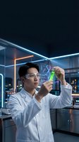 Young Asian male scientist in lab coat examining green liquid sample in test tube at modern research facility with digital displays and futuristic lighting.