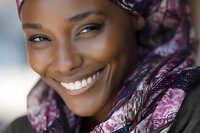 Close-up portrait of smiling African woman wearing purple patterned headscarf, showcasing bright white teeth and natural beauty in soft lighting.