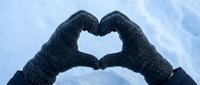 Hands in gray knitted mittens forming a heart shape against a snowy winter sky, symbolizing love, warmth, and the cold season.