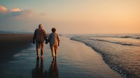 Senior couple walking hand in hand along beach shoreline at sunset, silhouetted against golden sky and gentle waves, creating romantic peaceful moment.