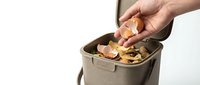 Hand dropping eggshell into a compost bin filled with kitchen scraps, promoting sustainable waste management and eco-friendly living.