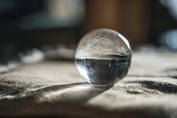 Crystal glass sphere resting on textured fabric surface with soft natural lighting creating reflections and shadows for meditation and mindfulness concepts.