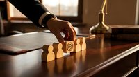 Businessman placing wooden block with target symbol among human figure pieces on office desk, concept of leadership and strategy.