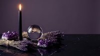 Mystical dark altar with burning black candle, crystal ball, amethyst crystals, and dried lavender on marble surface against purple background.