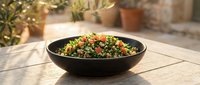 Vibrant tabbouleh salad with fresh herbs, tomatoes, and grains served in black bowl on wooden table outdoors for food photography and culinary content.