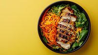 Sliced teriyaki chicken breast with sesame seeds served in black bowl with fresh carrot julienne and green salad on vibrant yellow background.