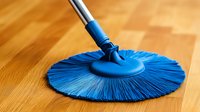 Vibrant blue circular mop head with bristles fanned out on wooden floor surface during cleaning process, showing household maintenance and hygiene concept.