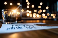 Business financial documents with pen on wooden desk featuring warm bokeh lights creating professional atmosphere for corporate analysis and planning.