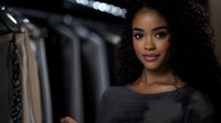 Young African American woman shopping for clothes in fashion boutique store with clothing racks in background for retail and lifestyle concepts.