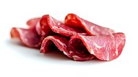 Thinly sliced raw beef meat curls arranged on white background, showing marbling and fresh red color. Premium quality meat cuts for culinary use.