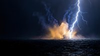 Dramatic lightning strike hits ocean surface creating explosive water splash and steam clouds against dark stormy sky for weather and nature concepts.