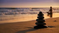Zen stone stack on beach at sunset with silhouette figure walking by ocean waves, meditation and mindfulness concept for wellness and spiritual balance.
