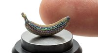 Miniature iridescent snake sculpture with rainbow metallic scales on circular platform next to human finger showing scale and craftsmanship detail.