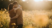 Romantic couple embracing in golden sunset light among wildflowers creating intimate moment for love and relationship concepts.