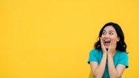 Excited young woman with dark hair and medium skin tone wearing turquoise shirt, hands on face expressing surprise and joy against bright yellow background for advertising and marketing campaigns.