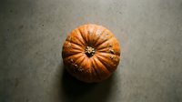Orange ribbed pumpkin on dark textured surface for autumn harvest decoration and seasonal cooking ingredients.