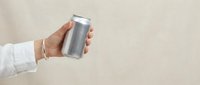 Hand holding aluminum beverage can against neutral beige background for product presentation and marketing materials.