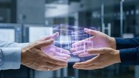 Hands exchanging digital holographic cube with glowing network connections in modern office environment, representing data transfer, technology collaboration, and business innovation.