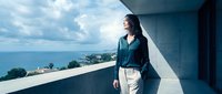 Young Asian businesswoman in elegant attire standing on modern balcony overlooking ocean view, professional lifestyle concept for corporate success.