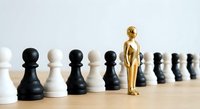 Golden figure standing out among black and white chess pawns on wooden surface representing leadership, uniqueness and strategic thinking in business.