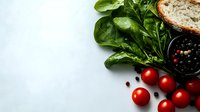 Fresh organic spinach leaves, ripe cherry tomatoes, black peppercorns, and rustic bread on white background with copy space. Food photography composition.