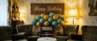 Vintage living room decorated for a birthday party with teal and gold balloons, retro radio, and a wooden Happy Birthday sign.