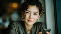 Young Asian woman with curly hair smiling warmly at camera in cozy indoor setting with soft natural lighting for lifestyle and portrait photography.