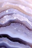 Purple agate crystal macro photography showing natural layered structure with druzy quartz crystals, mineral texture in soft pastel colors.