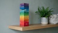 Colorful rainbow wooden block tower stacked on natural wood shelf next to green fern plant in modern minimalist interior design setting.