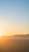 Serene mountain landscape at sunrise with warm golden light transitioning to cool blue sky, creating a peaceful dawn atmosphere suitable for backgrounds and wellness content.